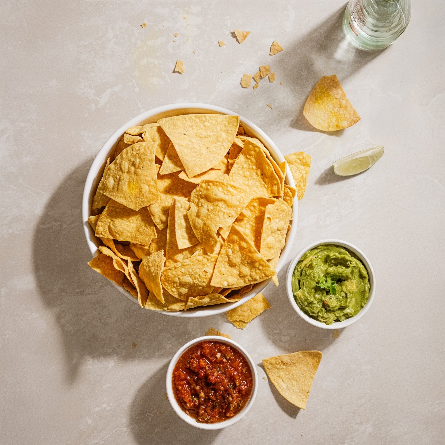 Tortilla chips with guacamole and salsa on a light surface
